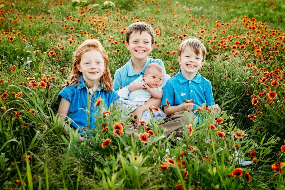 Children sit and laugh together in a vibrant field of red wildflowers and green grass on a sunny day in Fort Worth