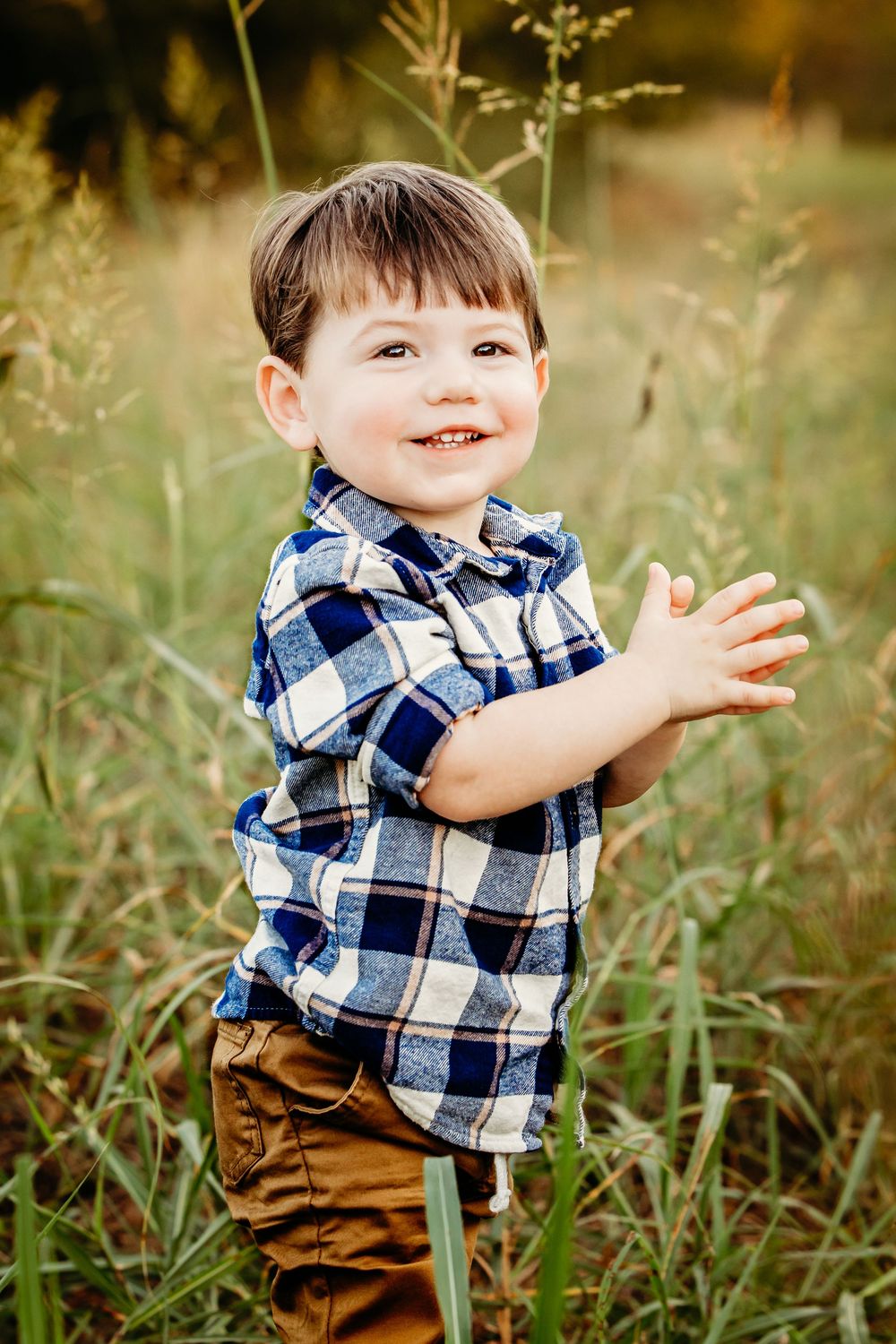Young child wearing blue plaid shirt and brown pants plays joyfully in a grassy field on sunny day in Fort Worth