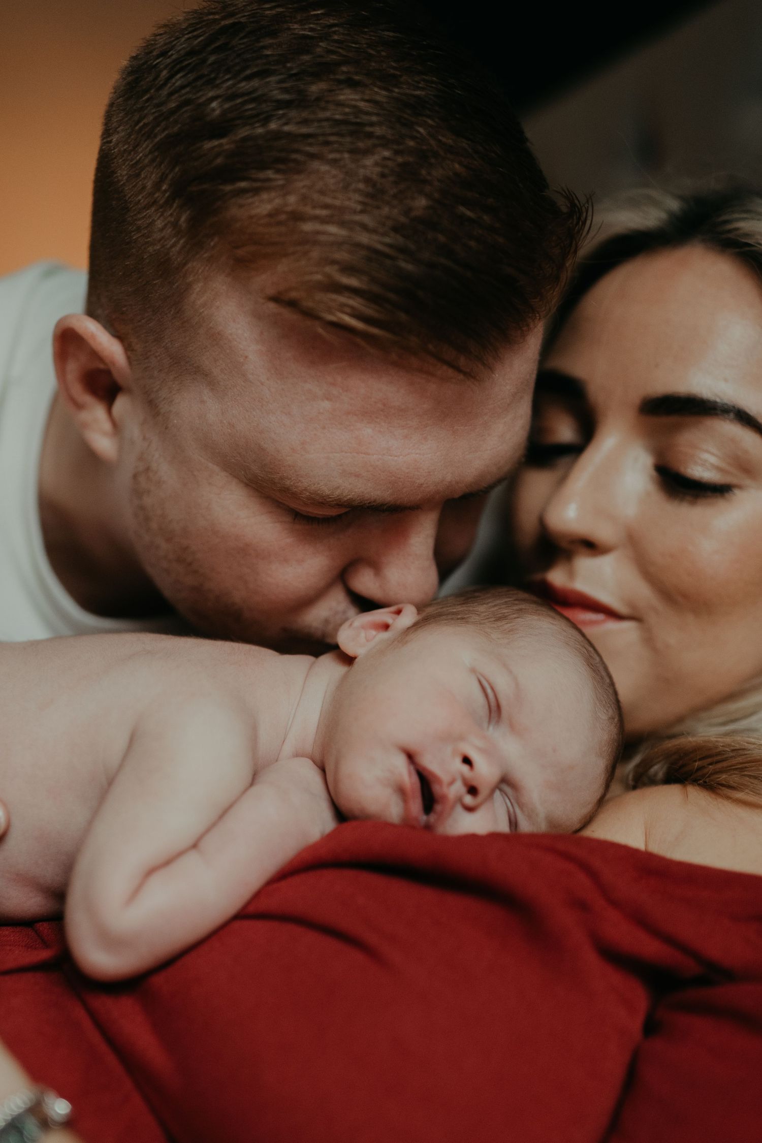 a couple with their new born baby the mother is looking at the baby while the father is kissing his head