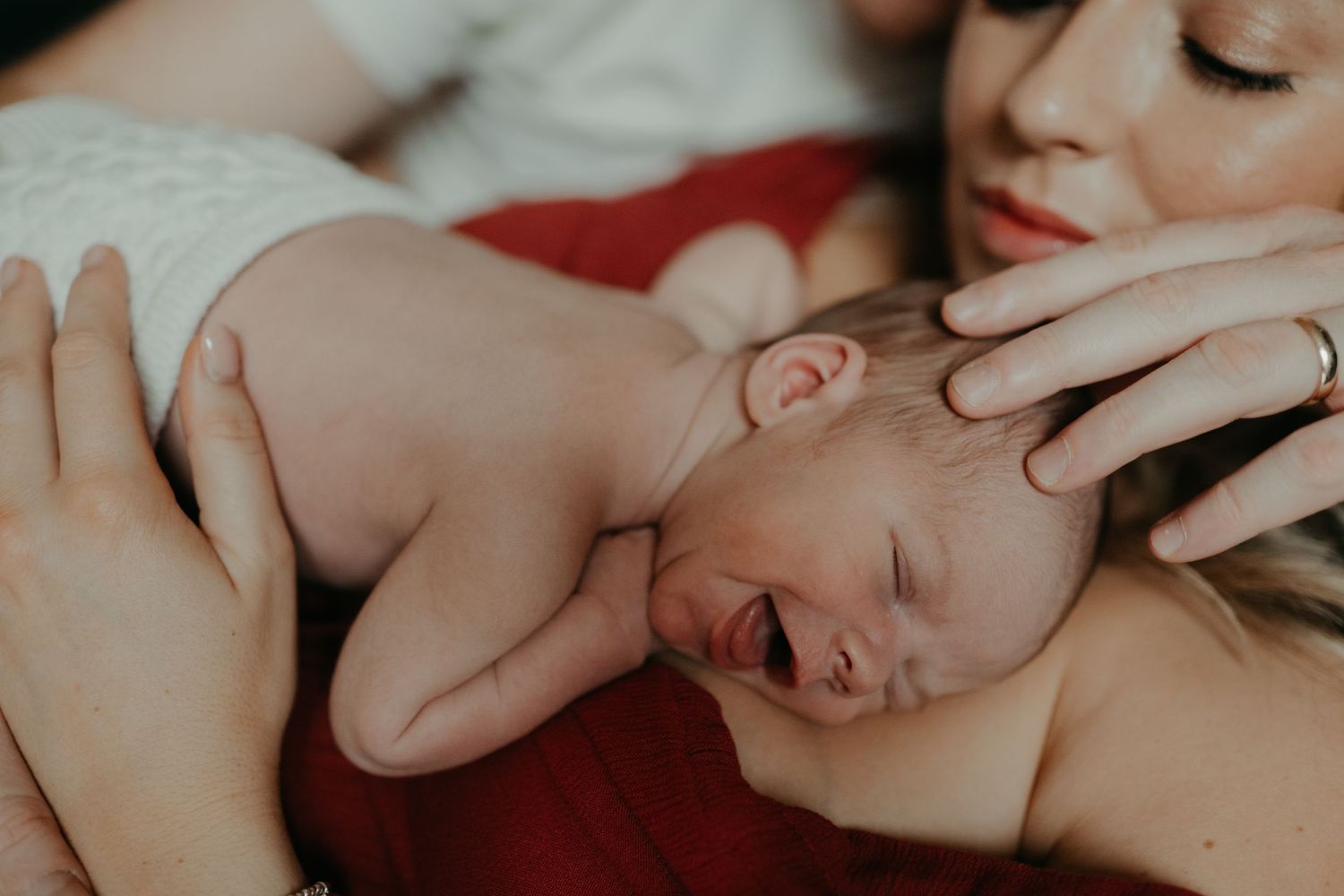 a detail shot of two parents touching their new born baby while the baby is smiling