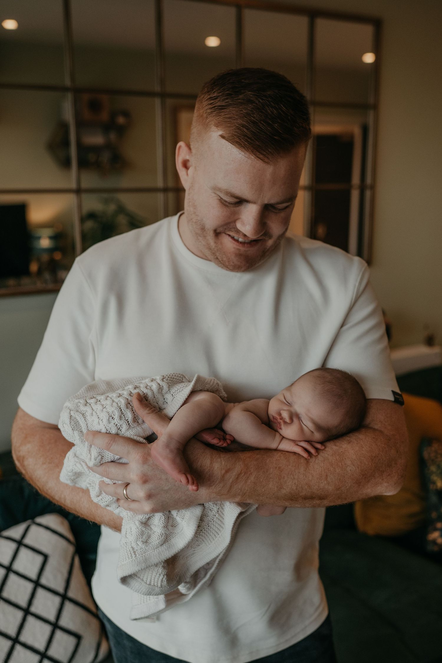 a father holding his new born baby in his arms is looking at him smiling