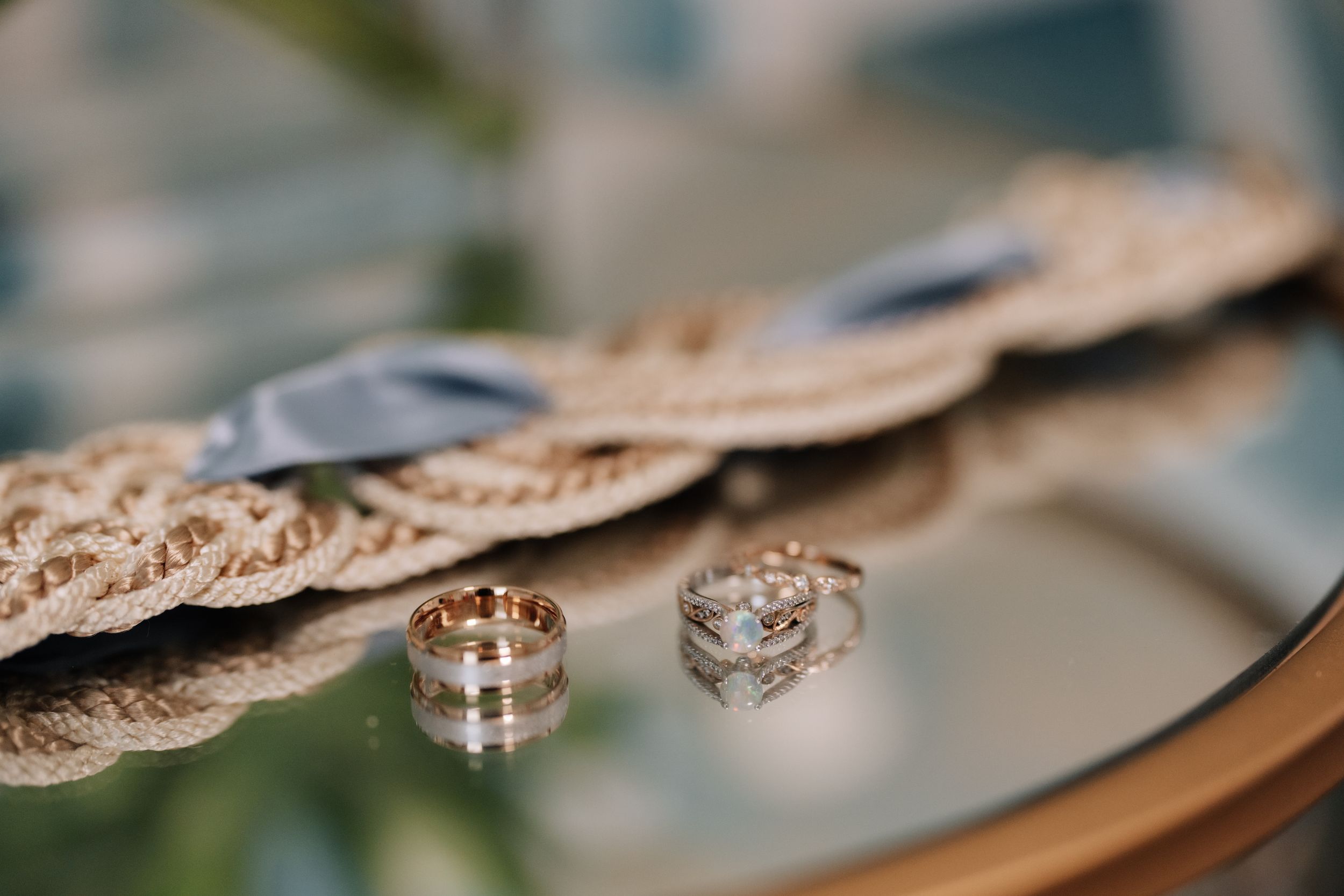 Delicate lace fabric with intricate floral patterns laid beside wedding rings on a reflective surface.