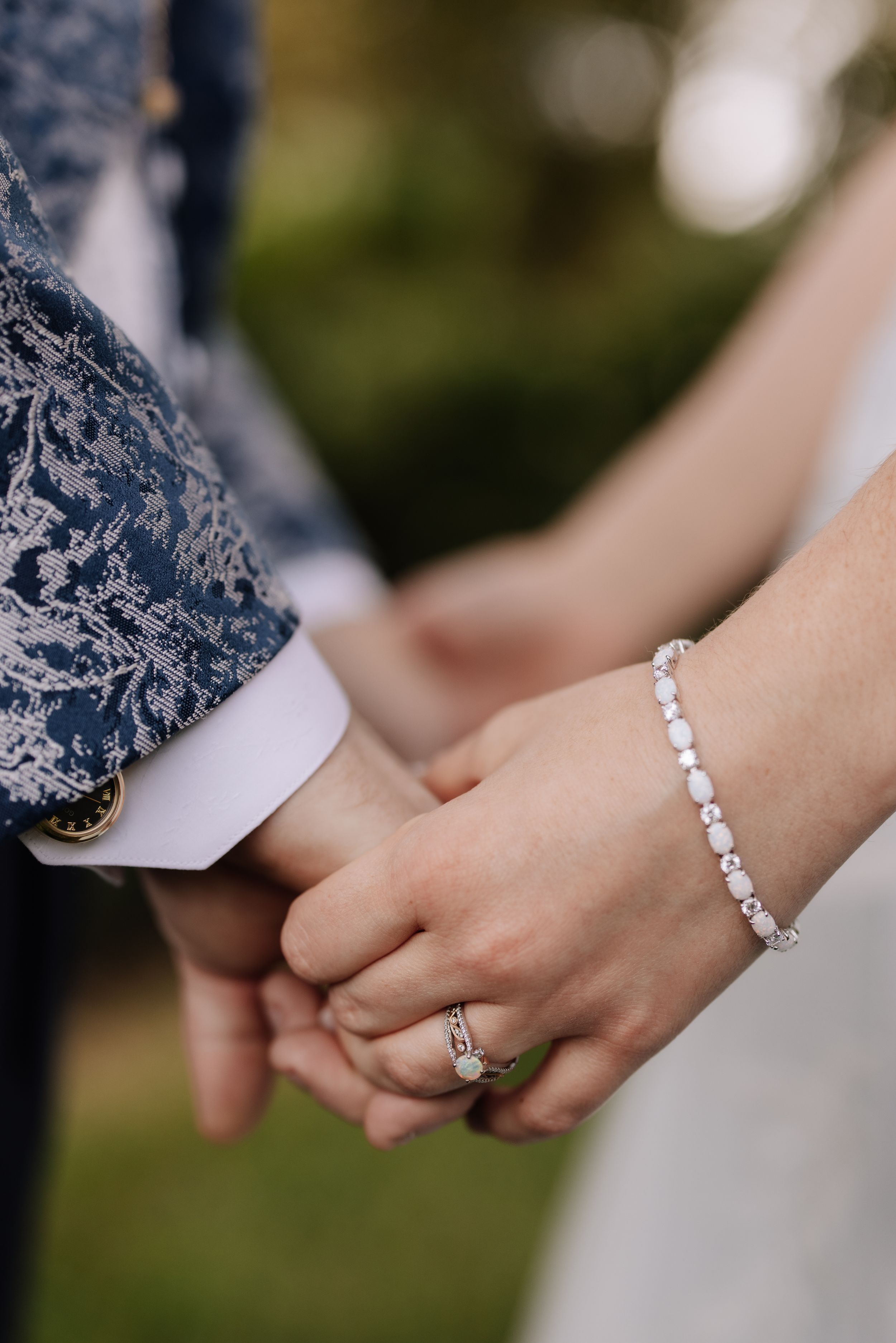 Close-up view of a couple's hands holding each other, showcasing a delicate bracelet and engagement ring.