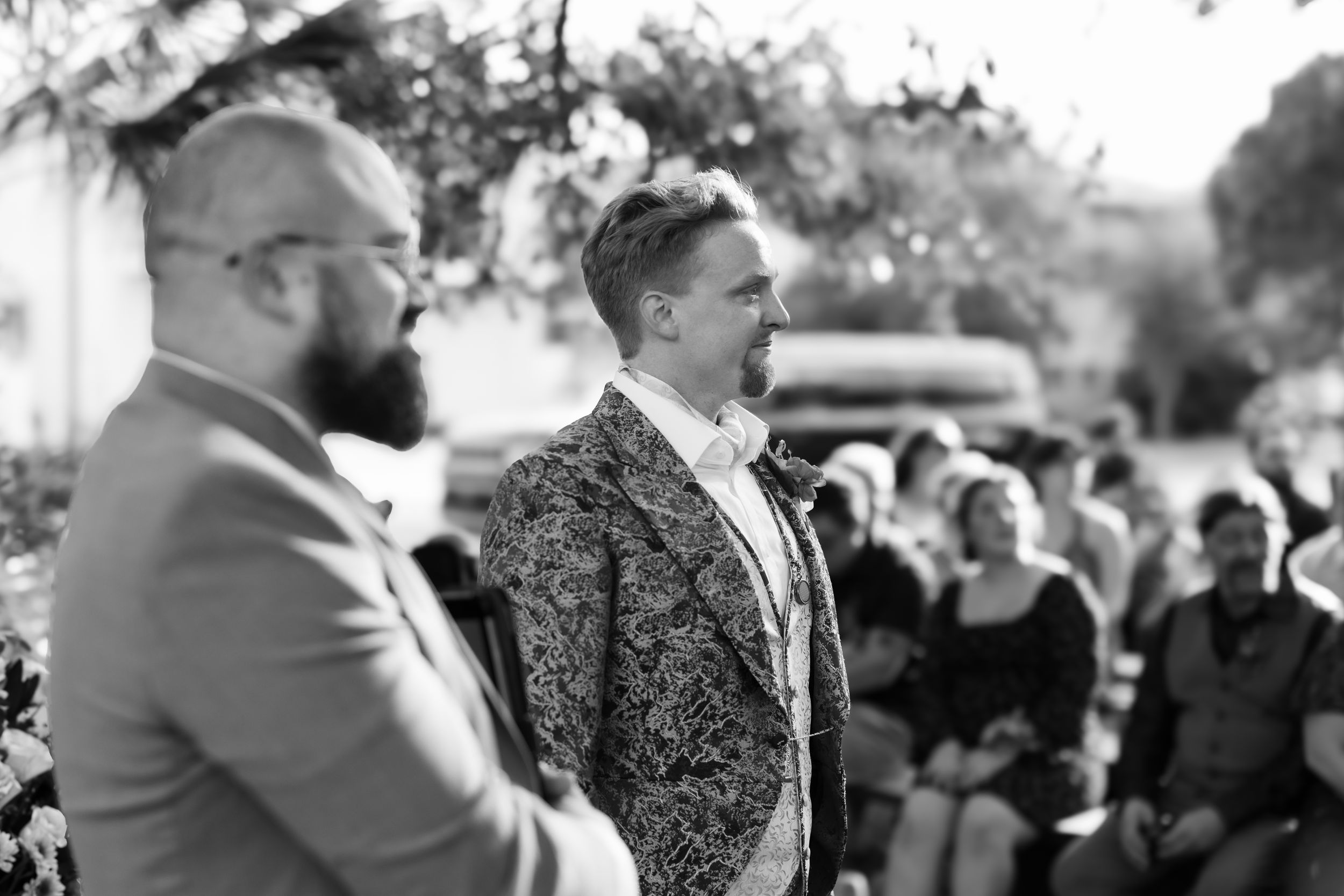 Black and white photo of an emotional outdoor wedding ceremony with two people standing at the altar and guests seated.