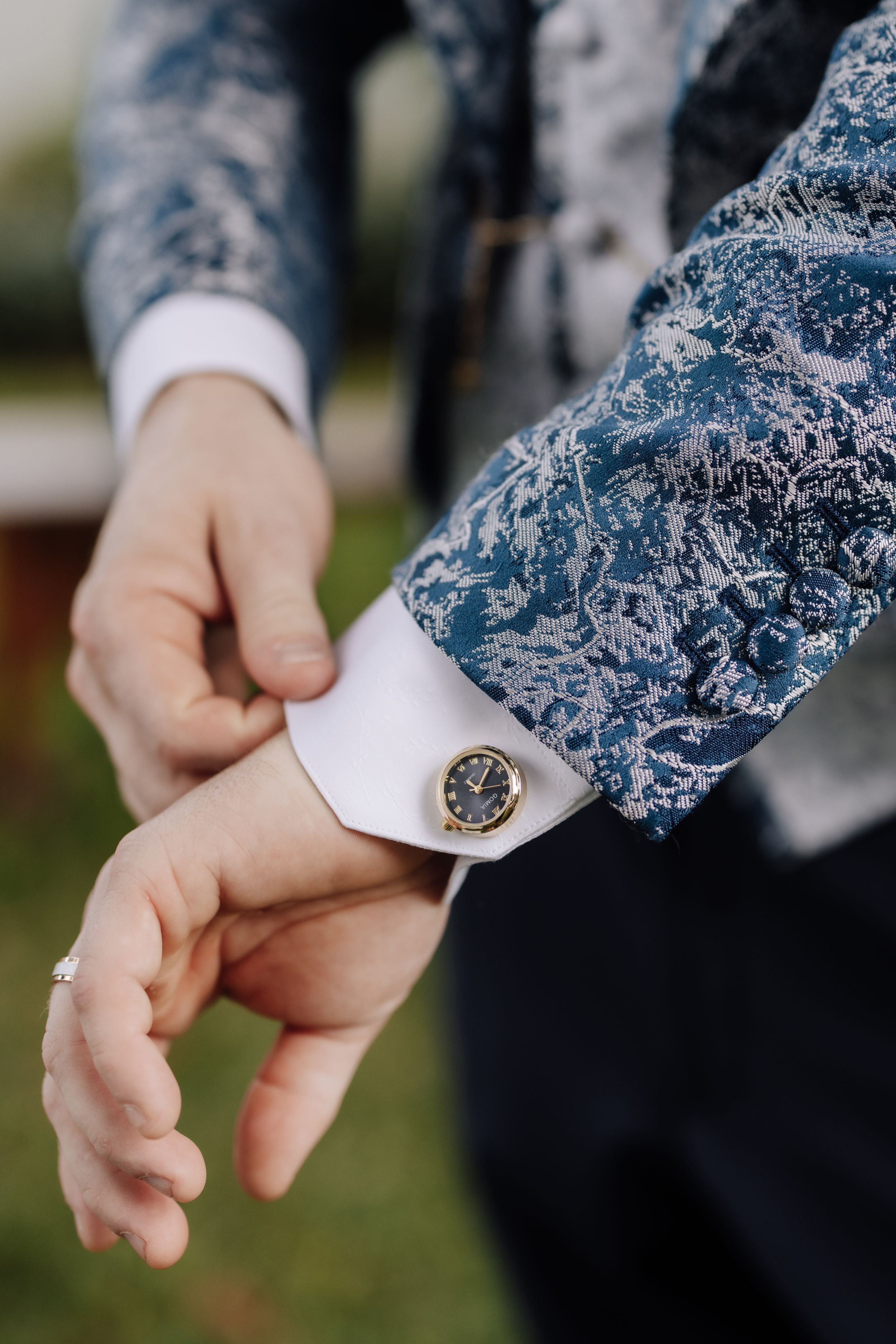 Close-up sequence showing hands adjusting a watch on a formal dress sleeve with blue floral pattern details.
