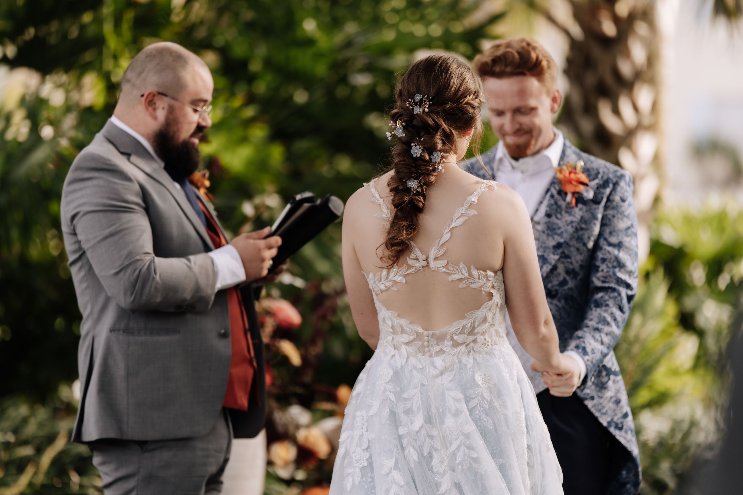 A couple shares a tender moment during their outdoor wedding ceremony in a sunlit garden setting.