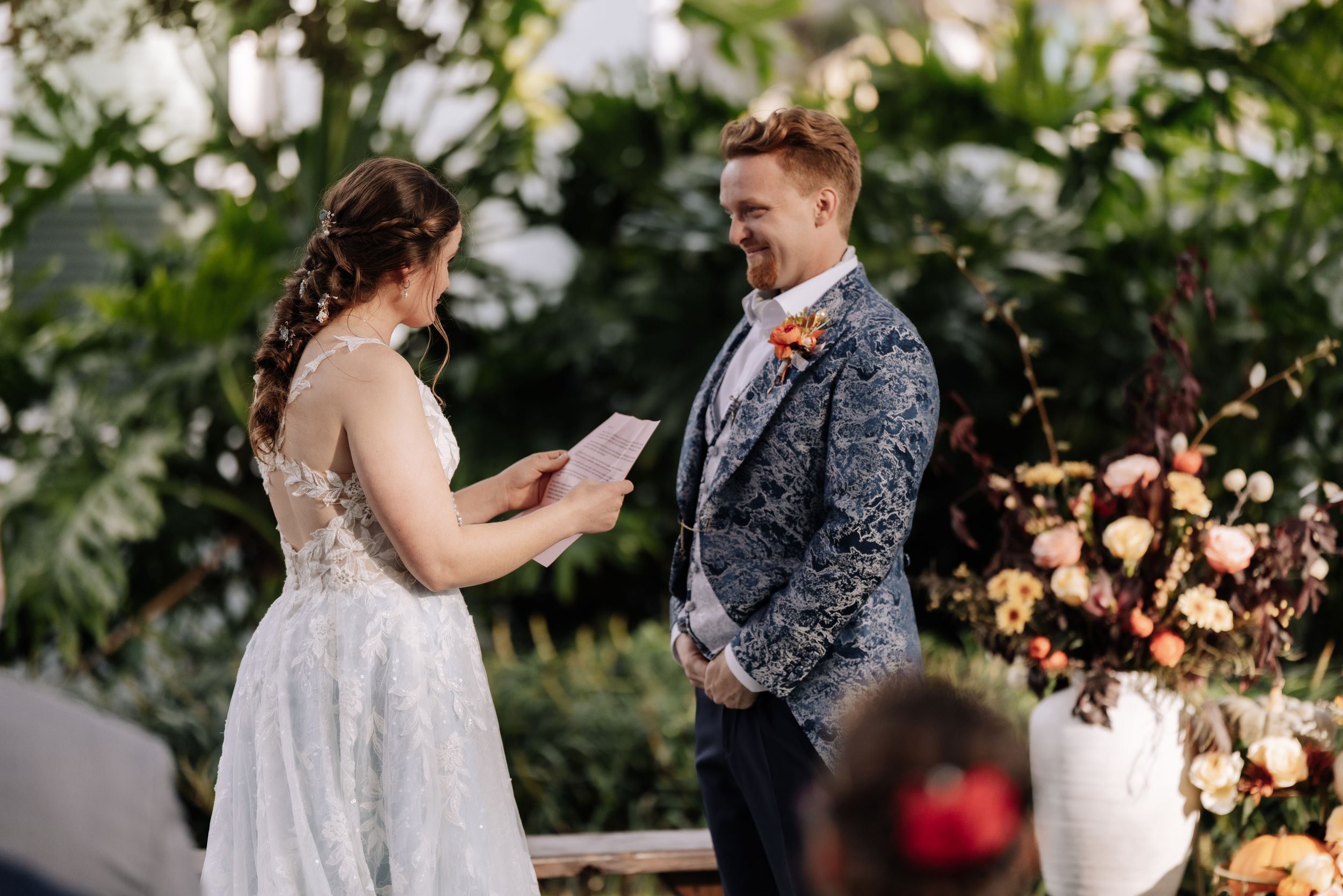 A couple shares a romantic moment during their wedding ceremony surrounded by lush greenery and floral decorations.