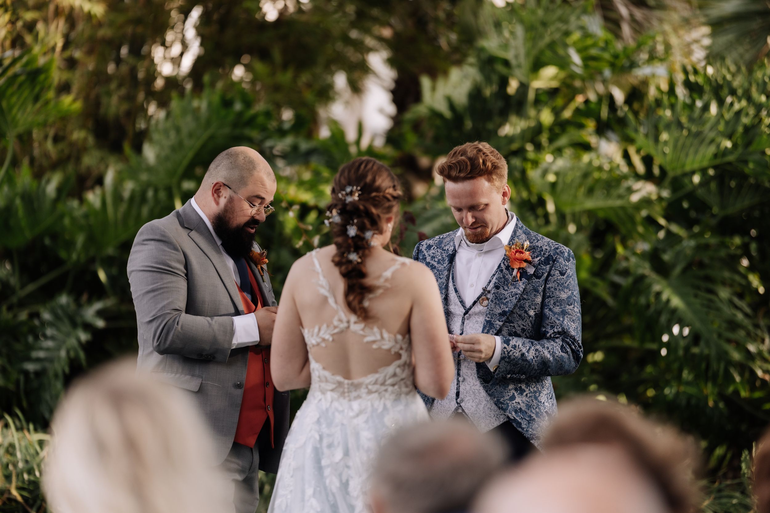 A romantic first look moment between a couple in formal wedding attire under lush green trees.