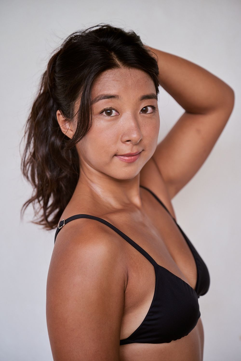A series of artistic portrait photos showing a person in a black bikini top posing against a light gray background.