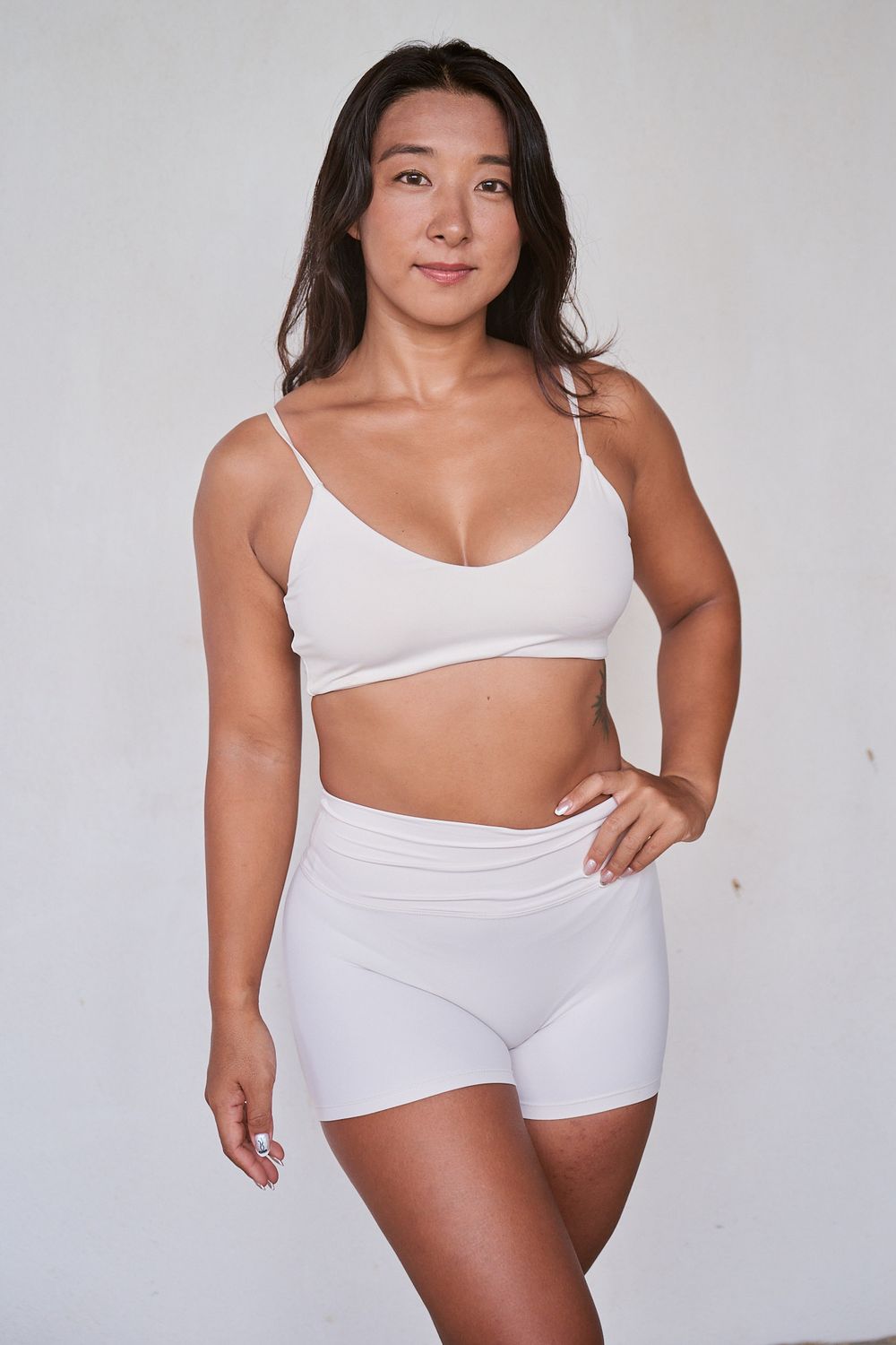 Model in white lingerie set poses confidently against neutral background showing body positivity and inclusivity.