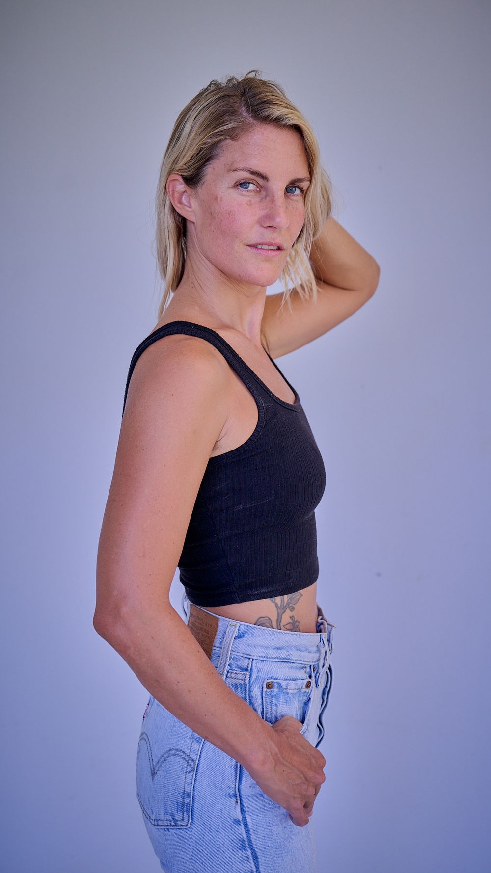 A series of poses showing someone wearing a black top and light denim jeans against a purple backdrop.