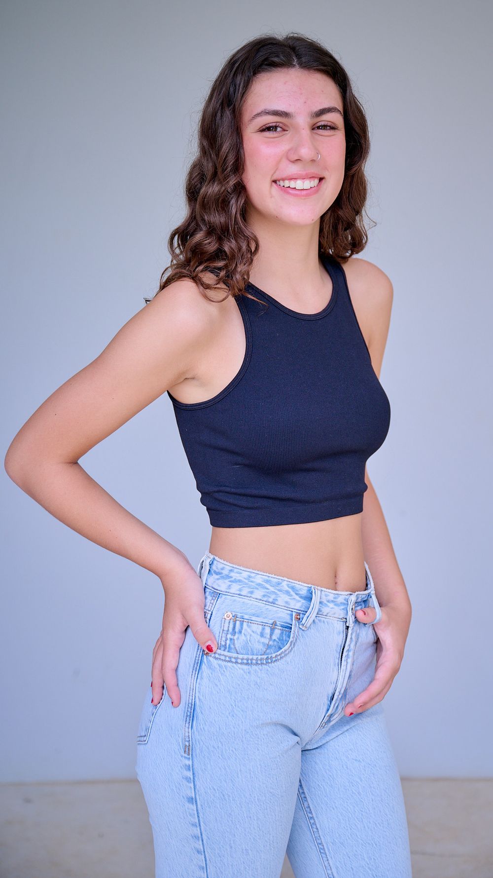 A person in a navy crop top and light wash jeans poses against a gray background in a series of casual photos.