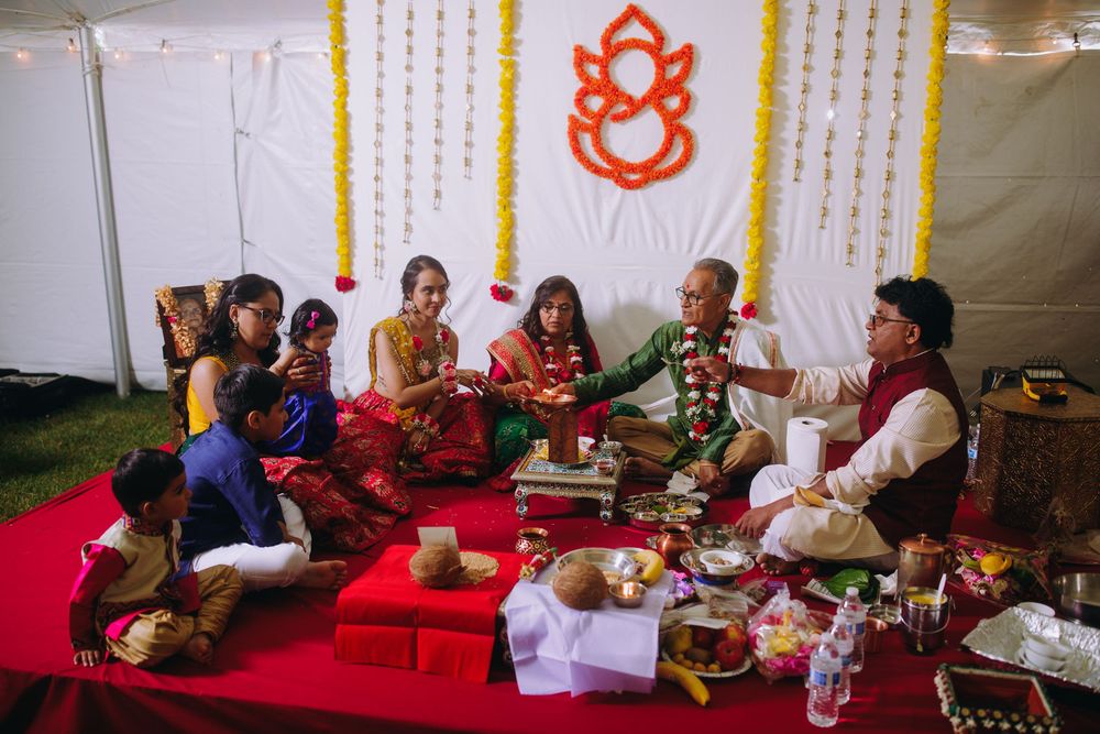 People gather on red carpets for a traditional Indian wedding ceremony in a decorated indoor venue.