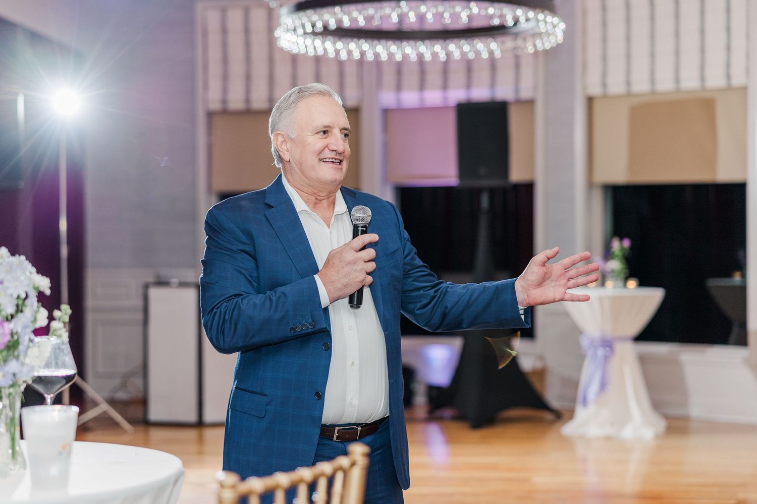Wedding guests dancing and celebrating at an elegant reception venue with circular chandeliers and pink lighting.