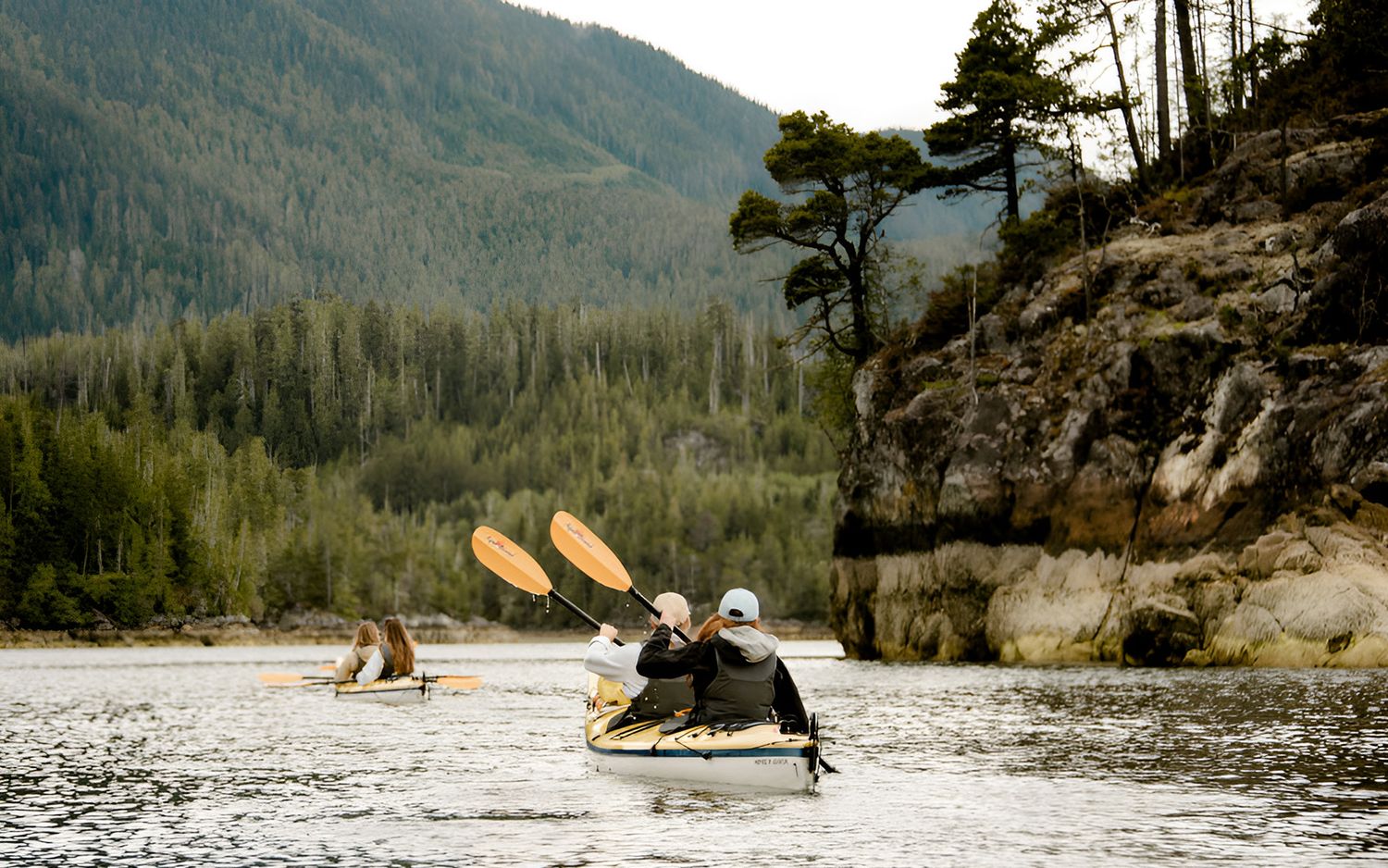 couple kayaks along shoreline with boulders and evergreen trees in Tofino