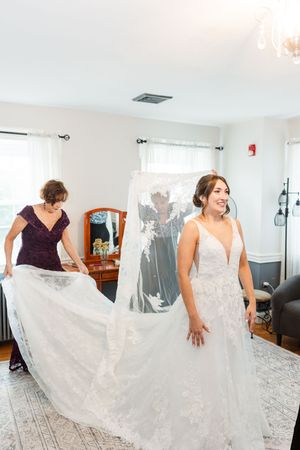 A flowing white wedding dress being arranged and styled in a bright room.