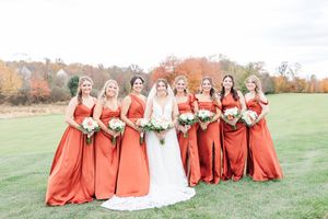Bridesmaids in rust-colored dresses standing with bride in outdoor fall setting.