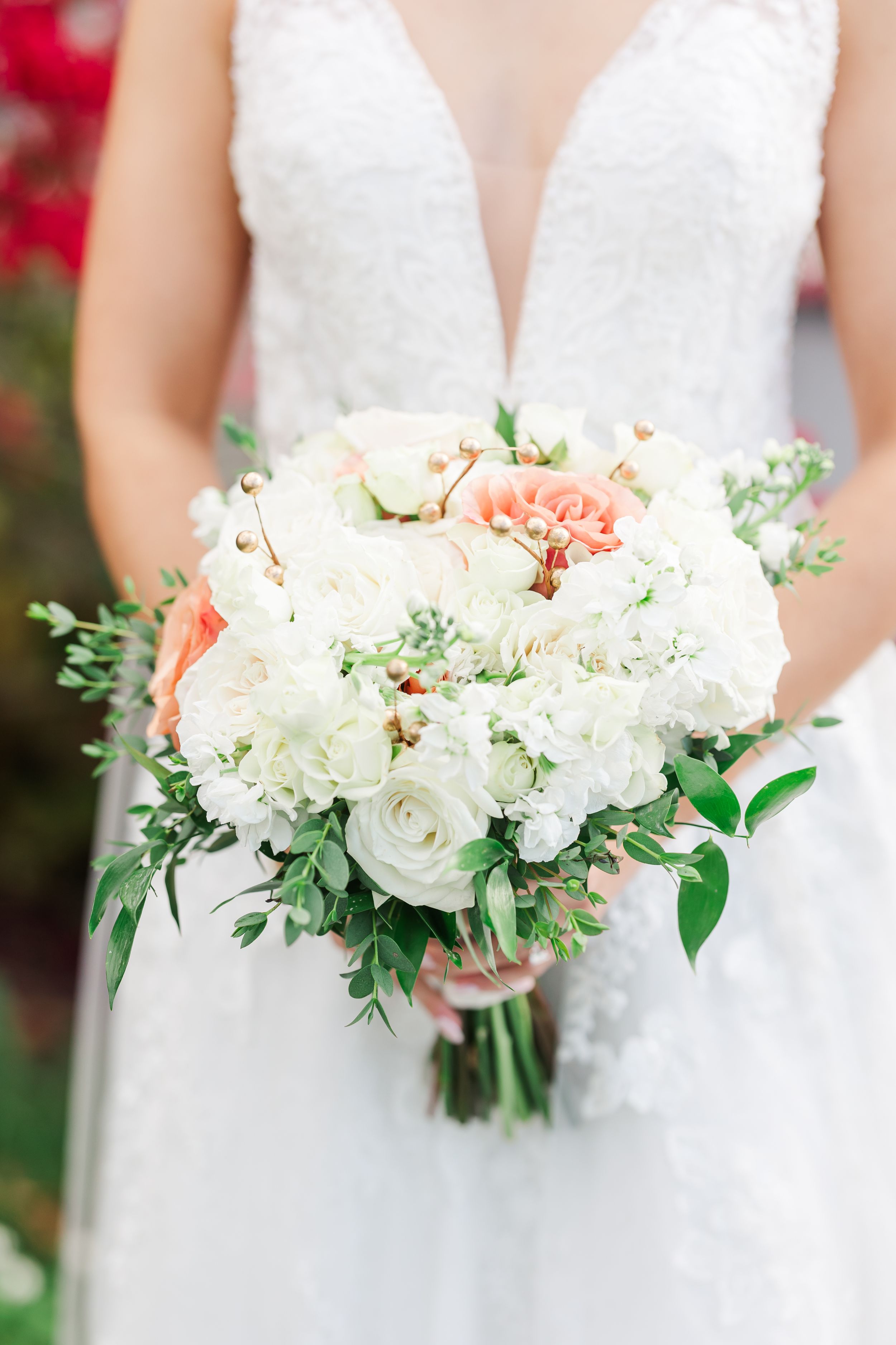 Elegant white and blush wedding bouquet with roses, peonies and greenery held against a white dress.