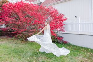 A white wedding dress flows in the breeze against a backdrop of vibrant red autumn trees.