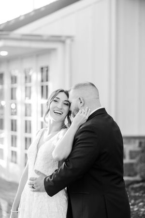 A black and white photo capturing a tender moment between newlyweds against a bright interior background.