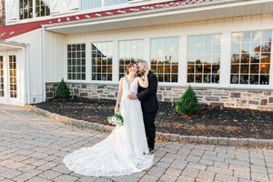 Wedding couple photographed along stone pathway outside elegant white venue.
