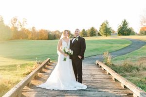Wedding couple walking along a wooden boardwalk path through an autumn field at sunset.