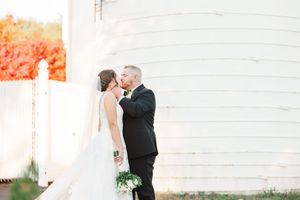 Couple embracing in front of a white rustic barn during an autumn wedding.