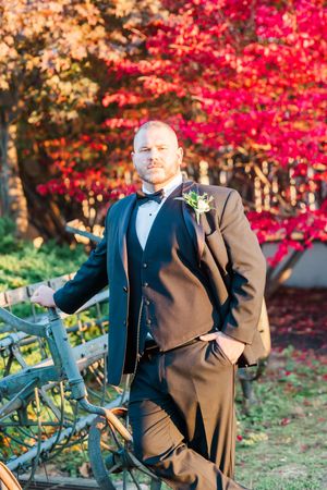 Wedding couple posing near vibrant red autumn maple trees and a park bench.