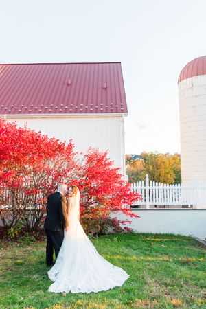 White barn wedding venue with dramatic red maple trees and white picket fence in autumn.