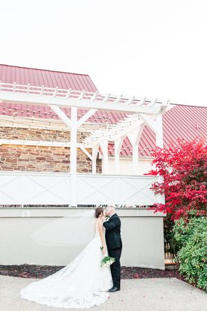 Wedding couple stands under white pergola with vibrant red autumn foliage.