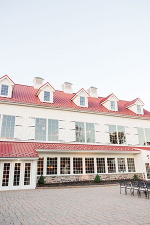 White wedding venue building with red roof and multiple dormer windows along a stone patio.