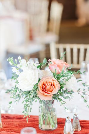Elegant table centerpieces with coral roses and greenery on red table runners.
