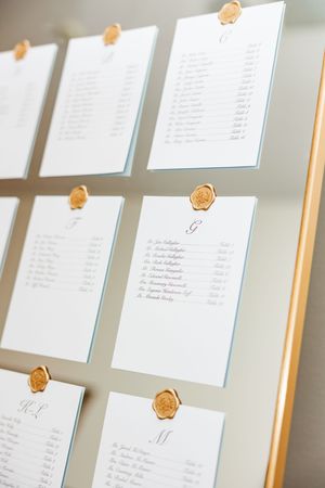Wedding seating chart display with white cards and wax seals mounted on a gray wall.