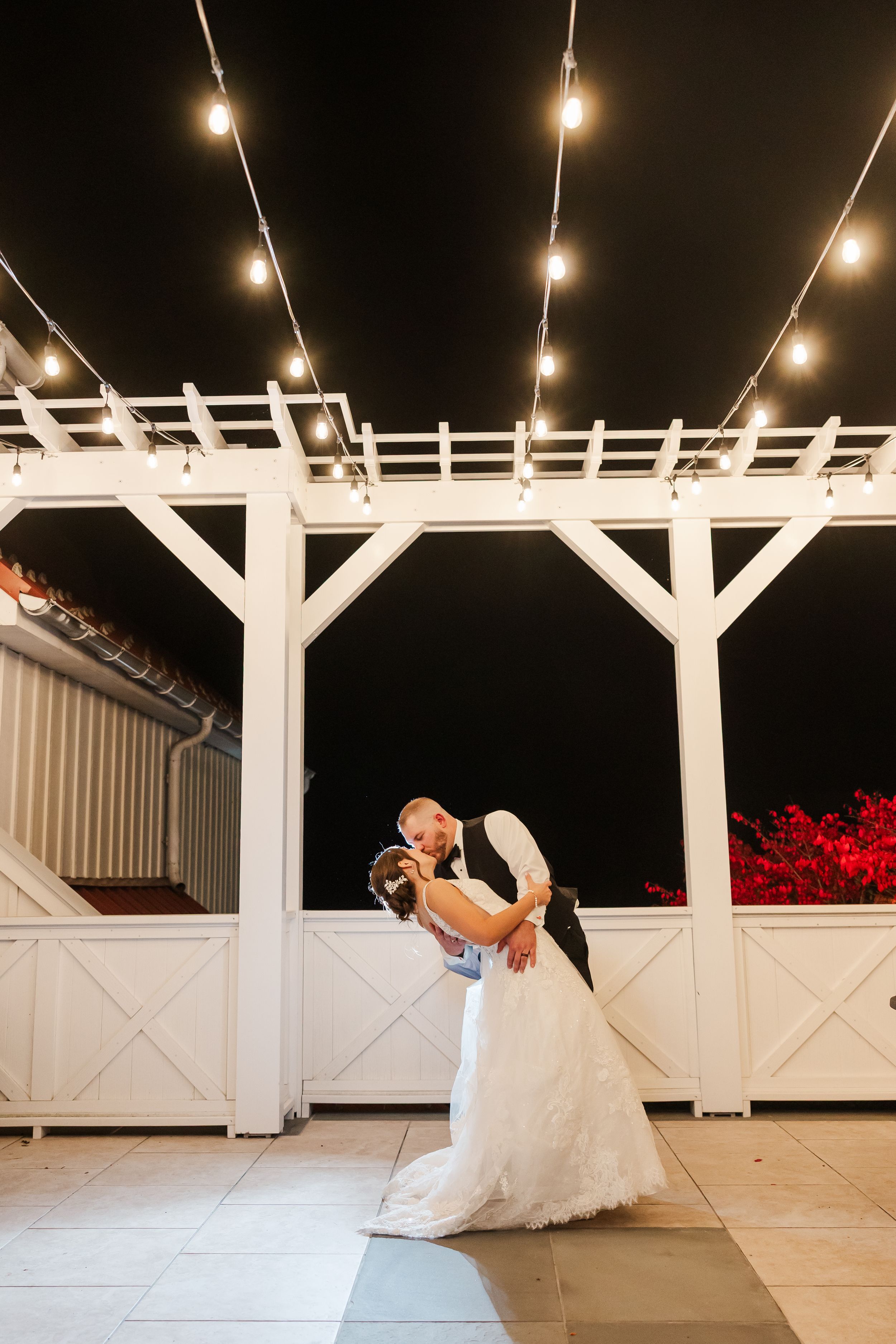 Romantic dance sequence under white pergola with string lights at outdoor wedding venue.