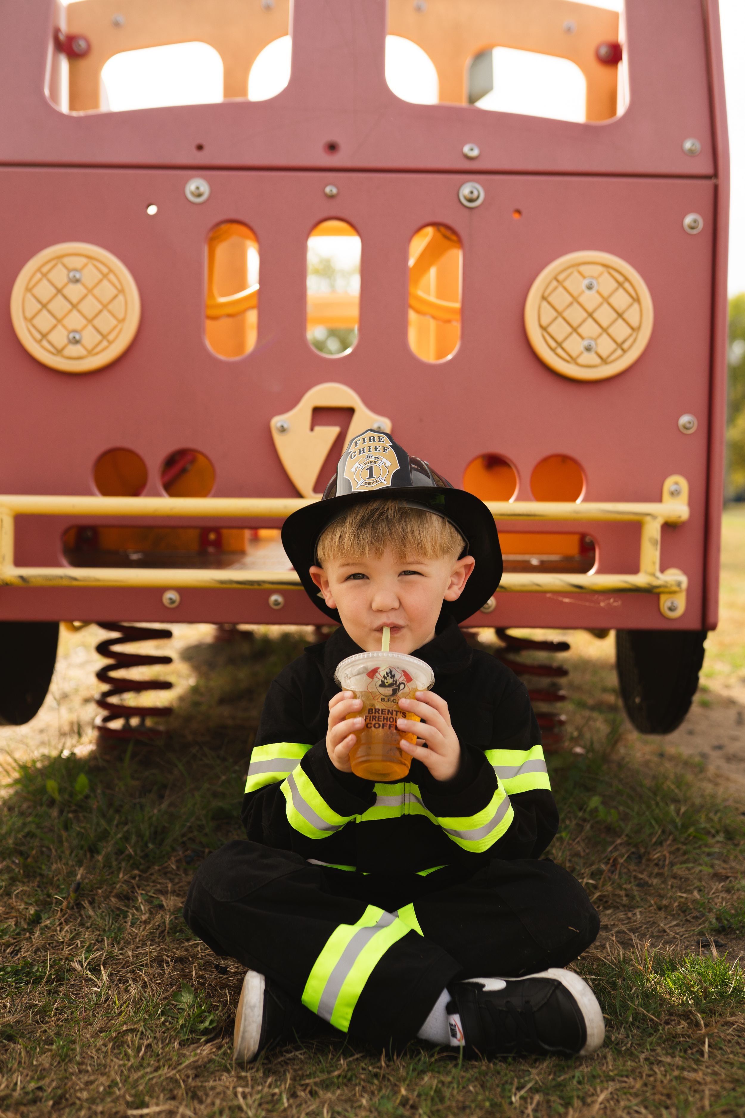 Small figure in firefighter costume and reflective gear sitting by playground equipment.