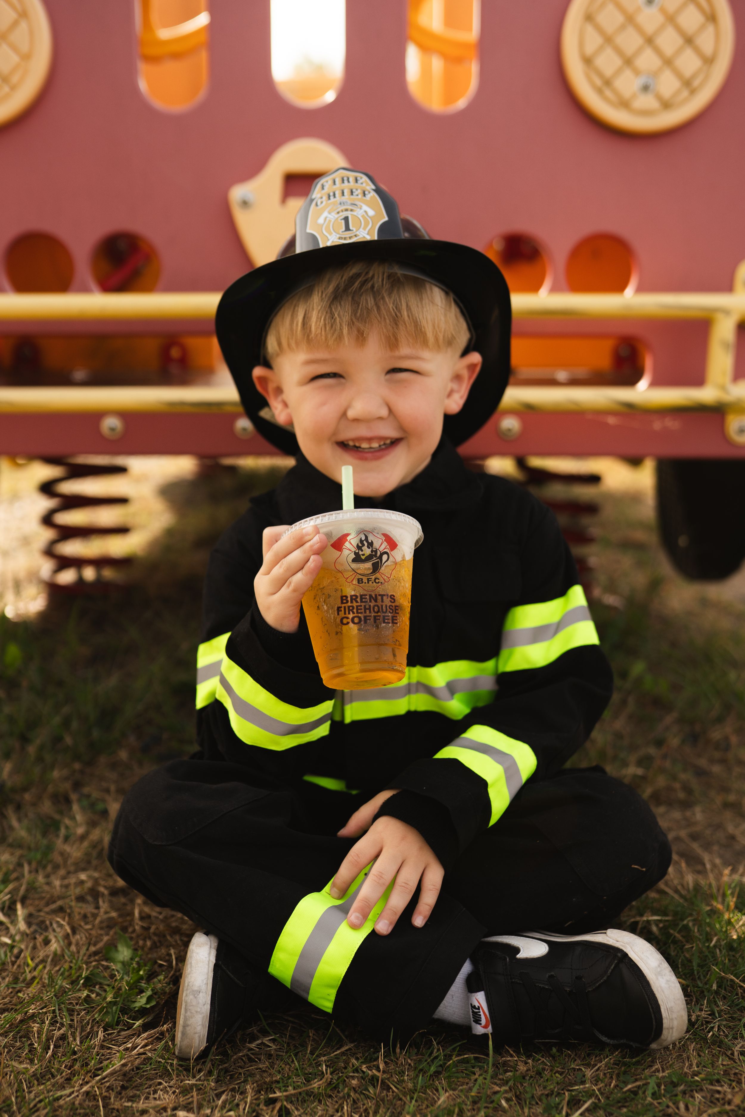 Small figure in black firefighter costume with reflective stripes sitting on grass.