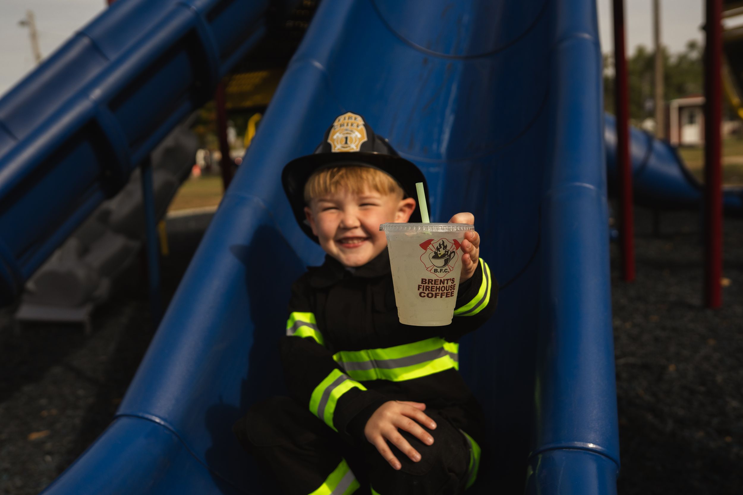Figure in firefighter costume playing near blue playground equipment.