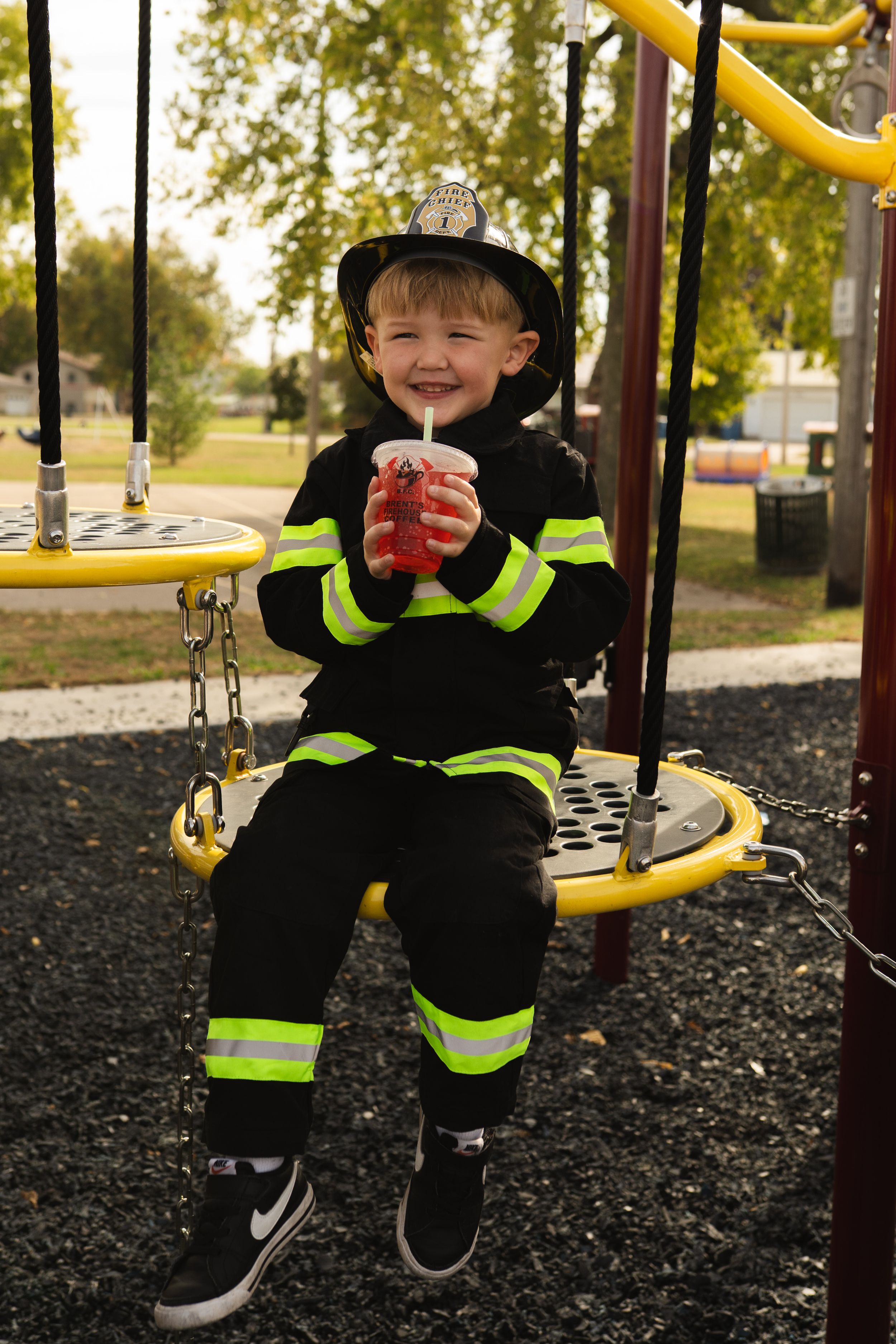 Figure in firefighter costume with reflective stripes sitting on playground swing.