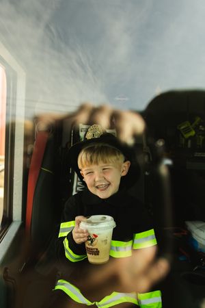 Child in safety vest enjoying a beverage in a vehicle interior.