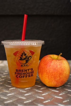 Orange-colored coffee drinks in branded cups next to a fresh apple.