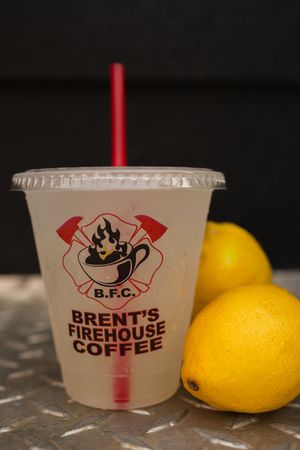 Clear branded coffee cups with red straws displayed next to yellow lemons.