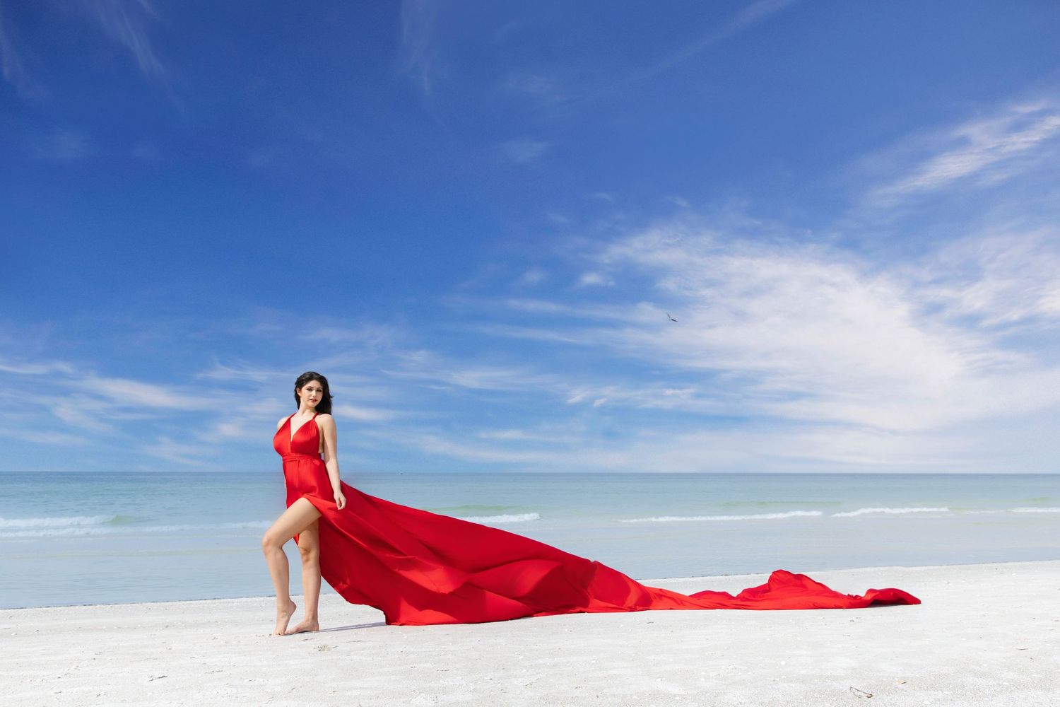 A figure in a flowing red dress walks across a stark white salt flat landscape under bright blue skies. Flying Dress Photoshoot