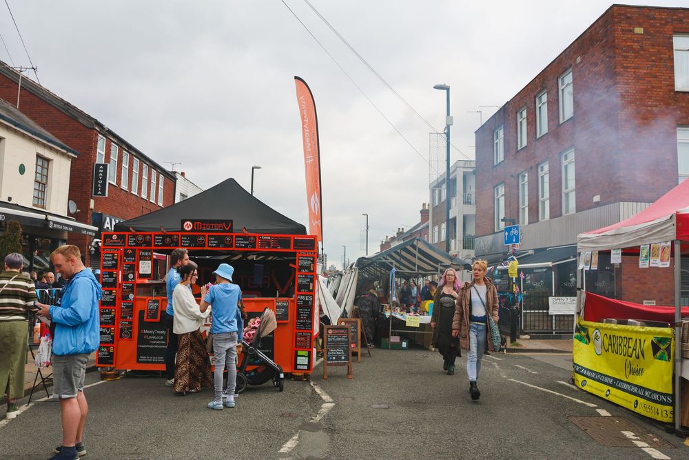 Busy outdoor street market in Earlsdon with food vendors, shoppers, and colorful stalls lining the road.