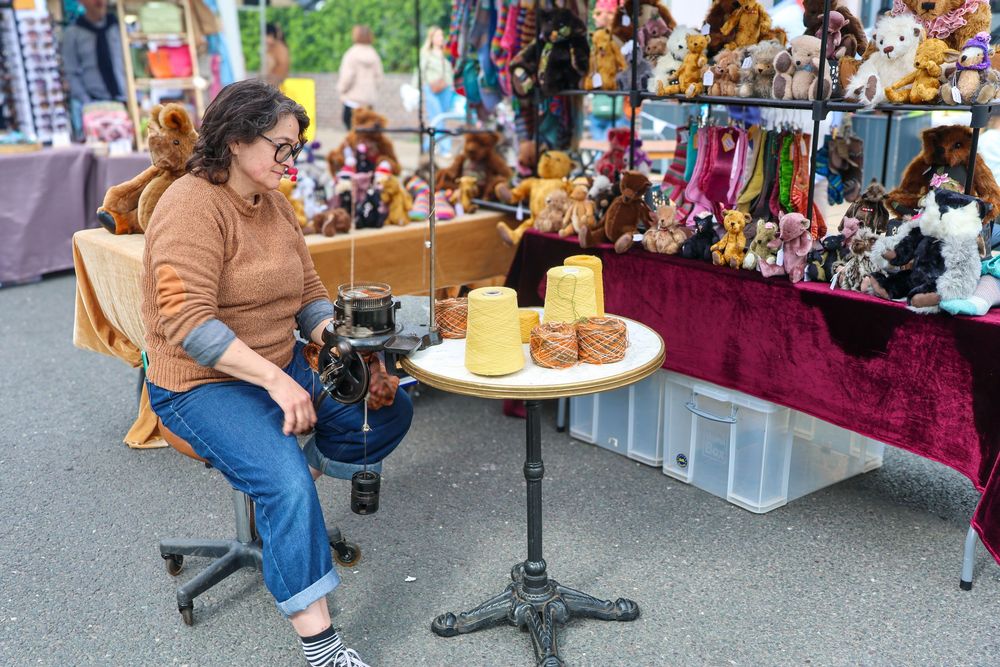 Woman sitting at a flea market stall surrounded by stuffed animals and toys for sale.
