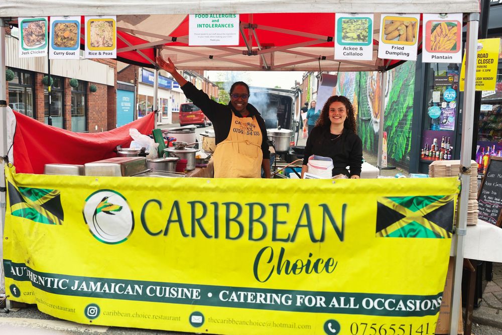 Caribbean Choice authentic Jamaican cuisine catering stall with two smiling vendors at an outdoor market.