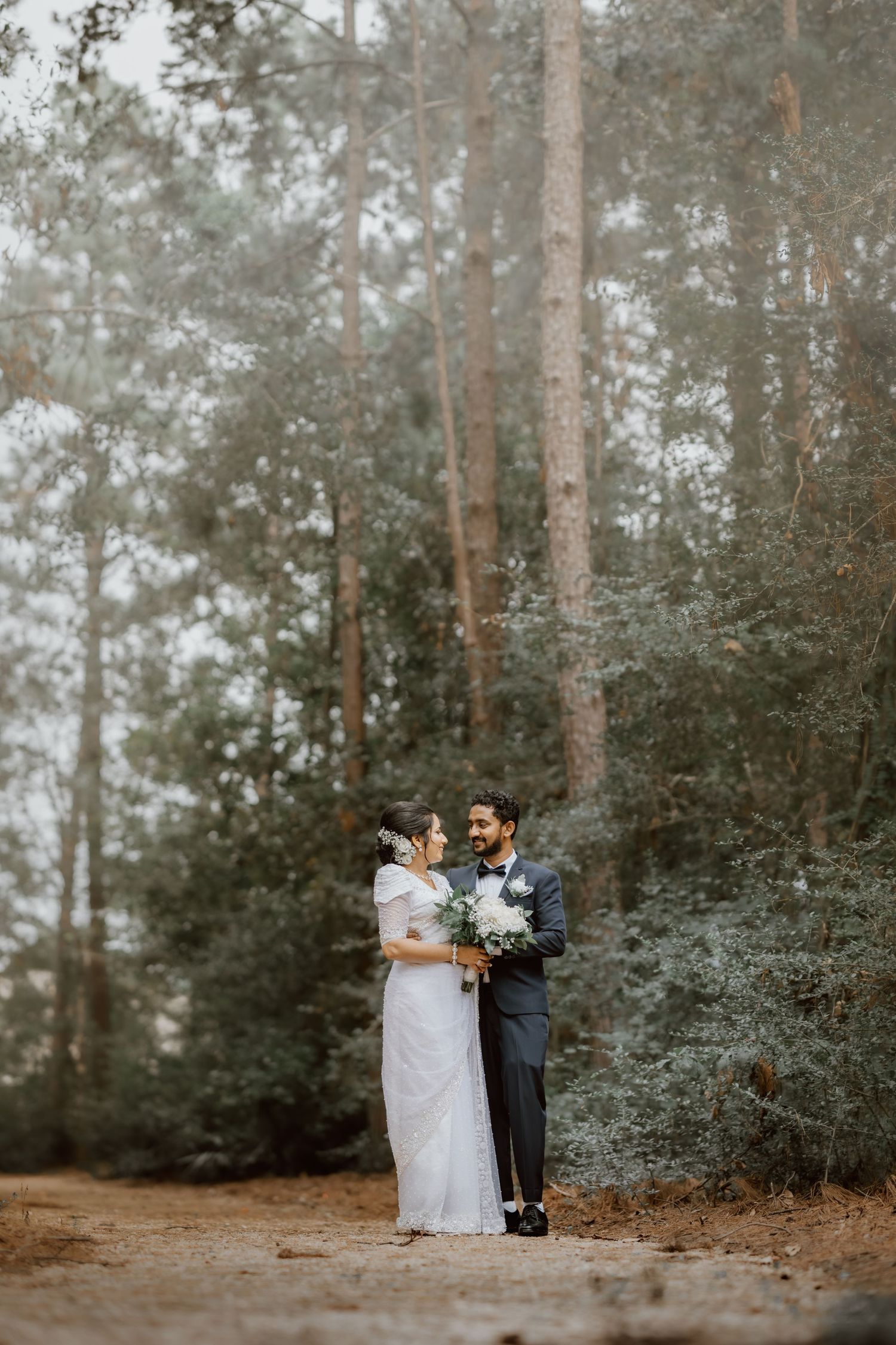 A romantic wedding couple embraces in a serene pine forest setting during their special day.