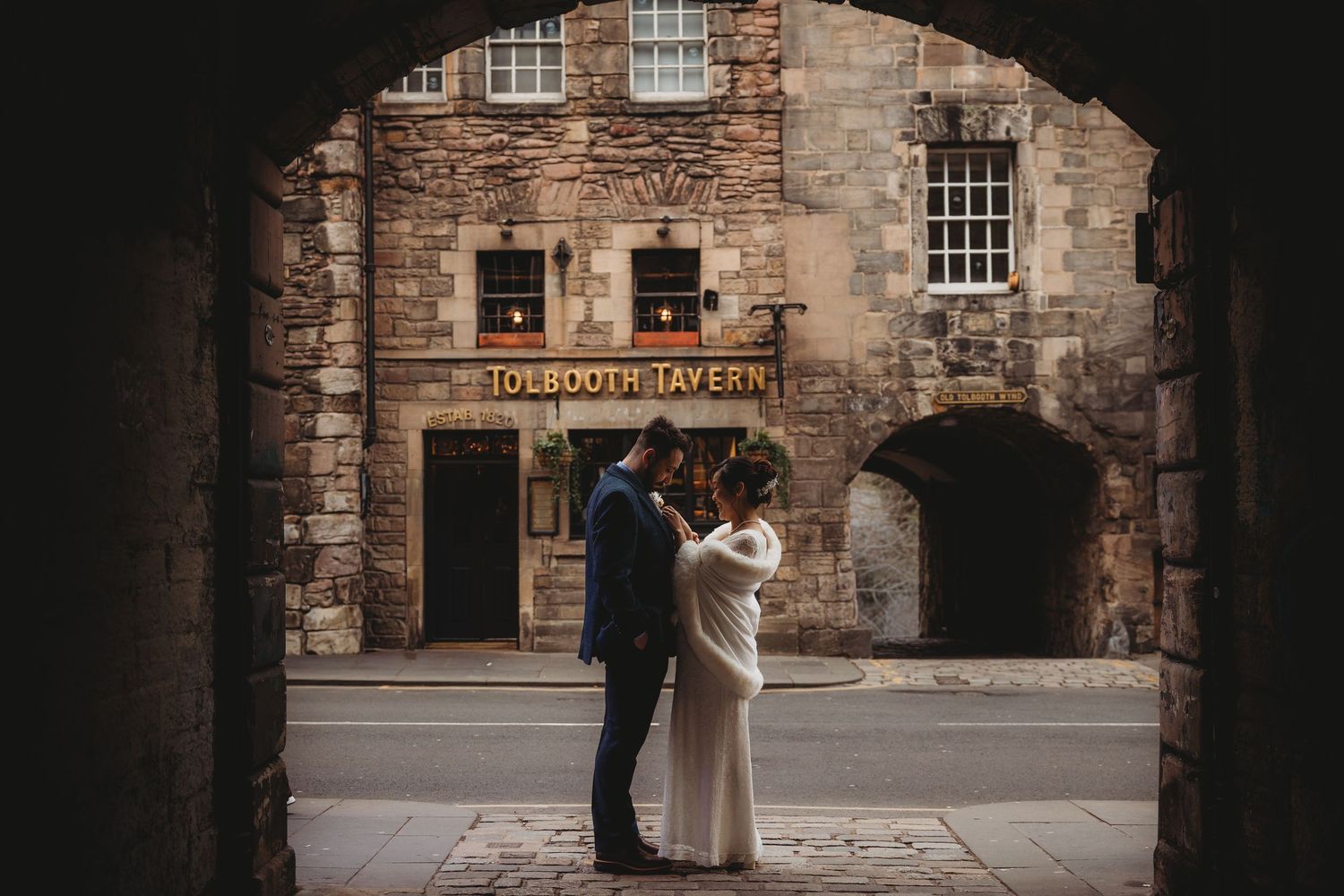 A romantic wedding couple embraces in front of a rustic stone building during their special day.