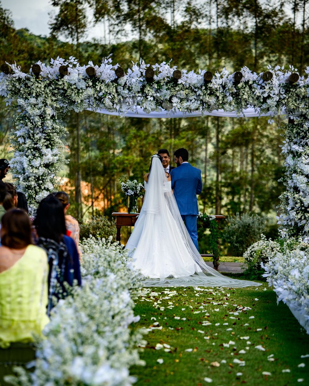 Romantic outdoor wedding ceremony under floral arch with white blooms lining the aisle.