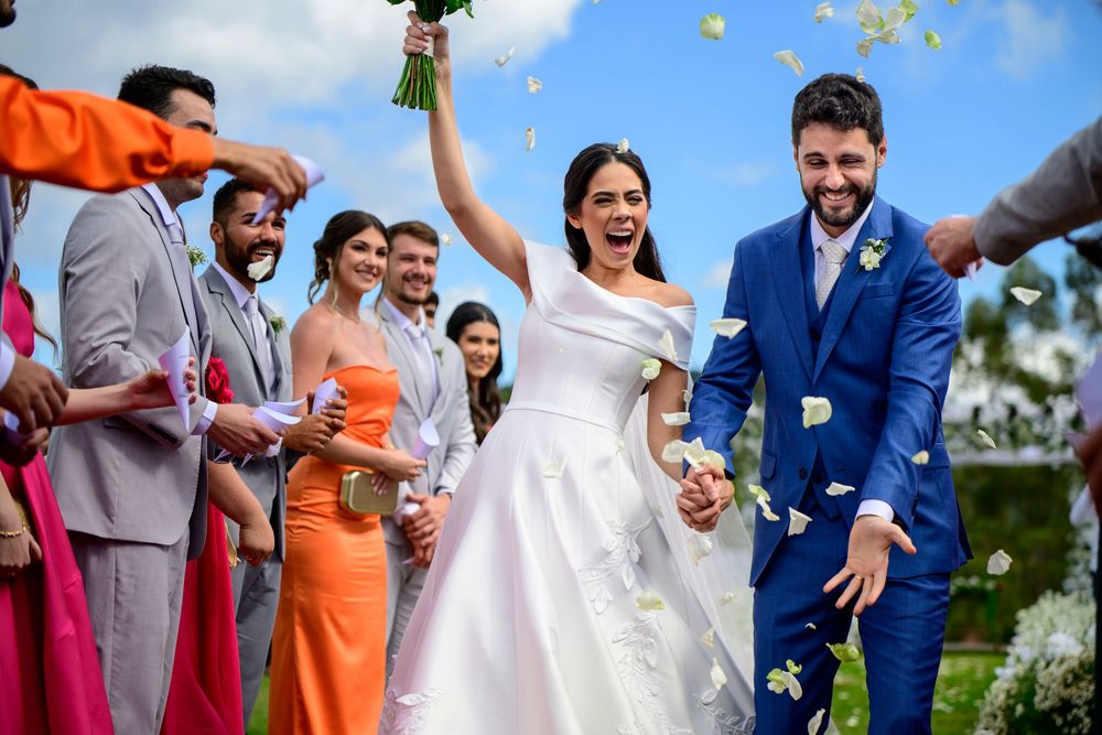 Joyful bride and groom exit ceremony as guests toss white flower petals outdoors.