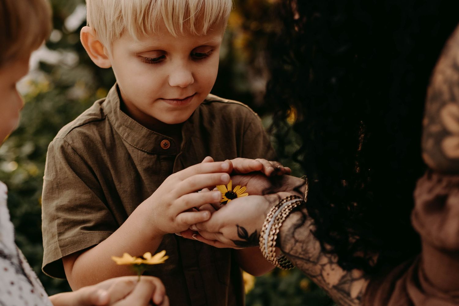 A young child in a brown coat holds and eats a chocolate chip cookie outdoors in warm natural lighting.